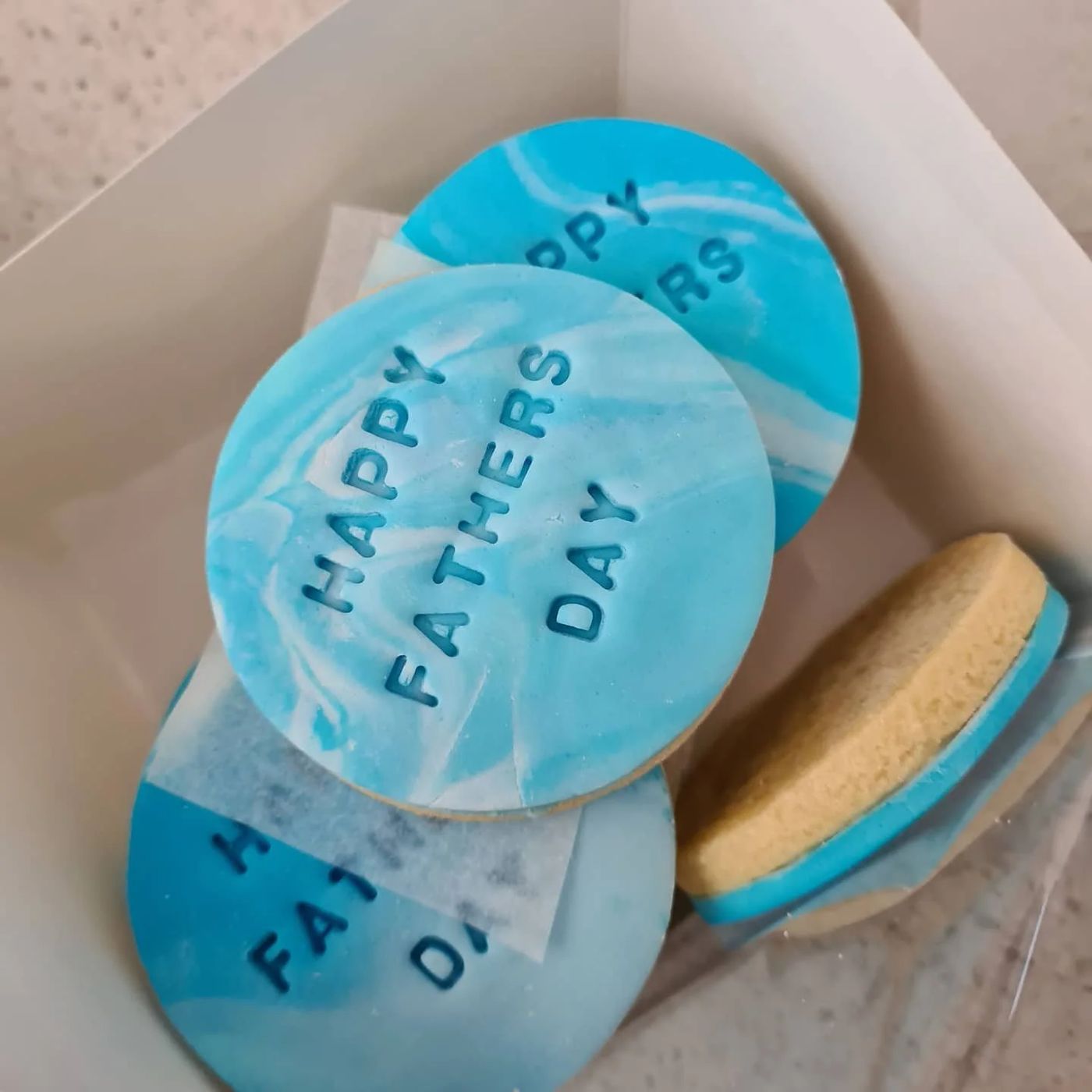 Marbled blue custom sugar cookies stamped with Happy Father's Day in a gift box
