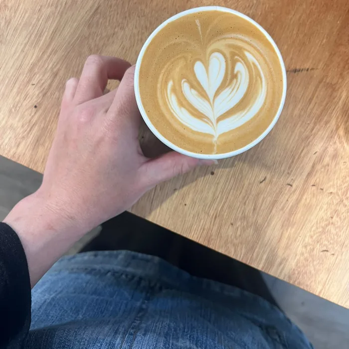 Latte with rosetta art held over a wooden table