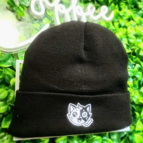 Black beanie embroidered with a Mini Misfits cat character in white, on a leafy green backdrop